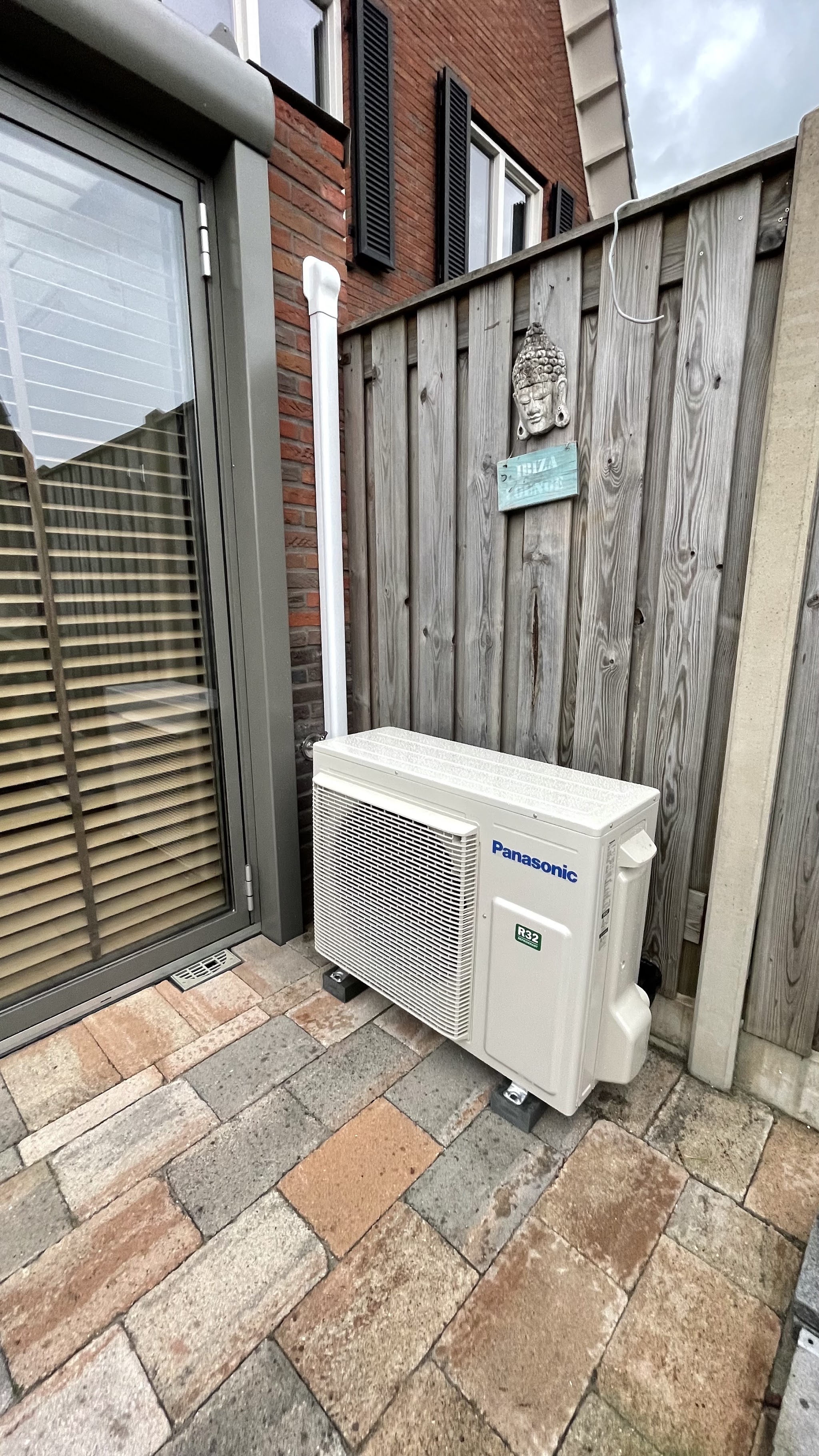 Panasonic buitenunit op een terras naast een houten schutting