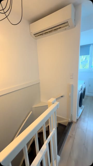 Witte binnenunit hoog aan de wand boven een trapgat
