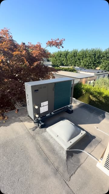 Warmtepomp buitenunit op een plat dak tussen de bomen